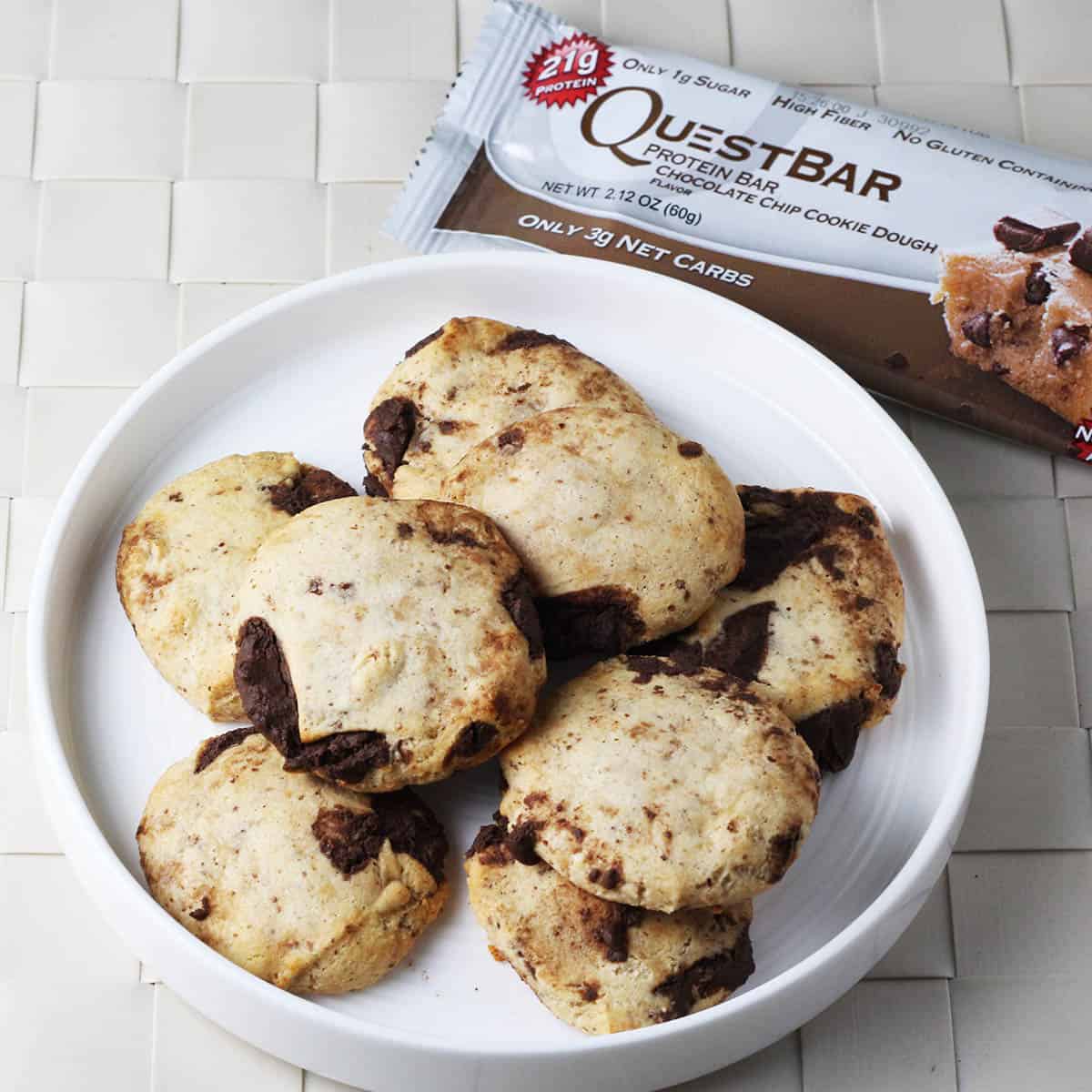 eight pieces of a chocolate chip cookie dough quest bar baked into cookies on a white plate and next to a packaged quest bar.