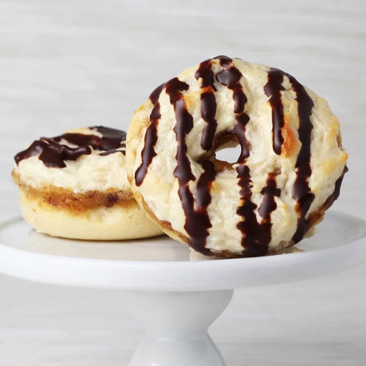 two mini donuts with chocolate drizzle on a small white cupcake stand