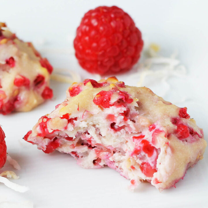 bitten coconut raspberry cookie - white cookie with bright raspberry pieces - with a fresh raspberry behind it all on a white plate