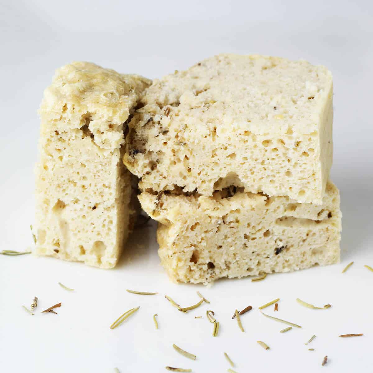 three small pieces of rosemary protein focaccia with dried rosemary sprinkled on the white plate