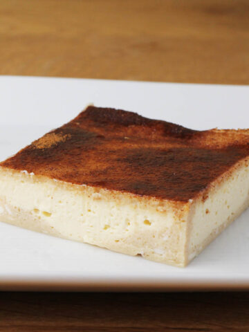 a square sopapilla cheesecake bar on a white plate on a wood table