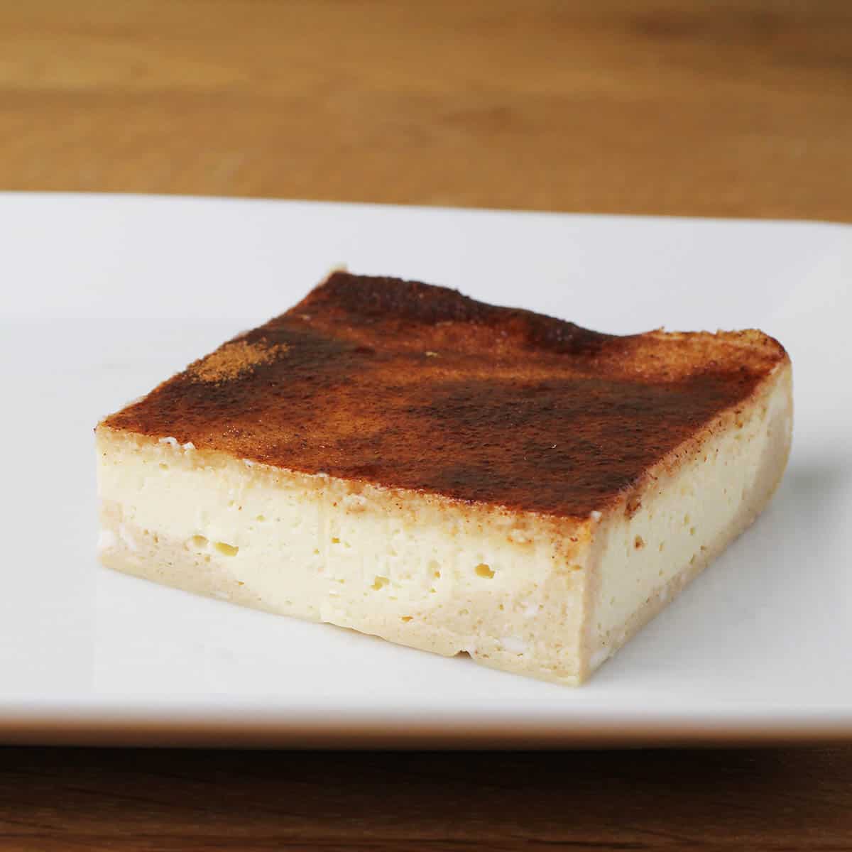 a square sopapilla cheesecake bar on a white plate on a wood table