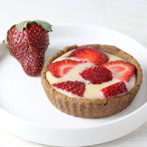 a strawberries and cream tartlet with a whole strawberry on a round white plate on a light background