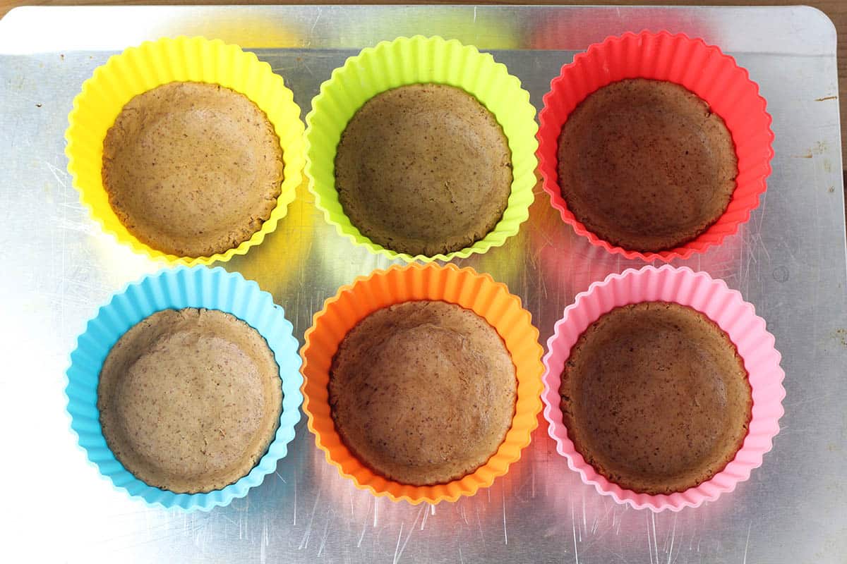 six large silicone muffin cups with unbaked crust on a silver baking sheet