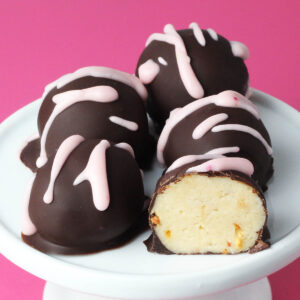 four whole and one half chocolate covered strawberry cheesecake protein balls with pink icing drizzle