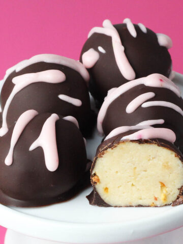 four whole and one half chocolate covered strawberry cheesecake protein balls with pink icing drizzle