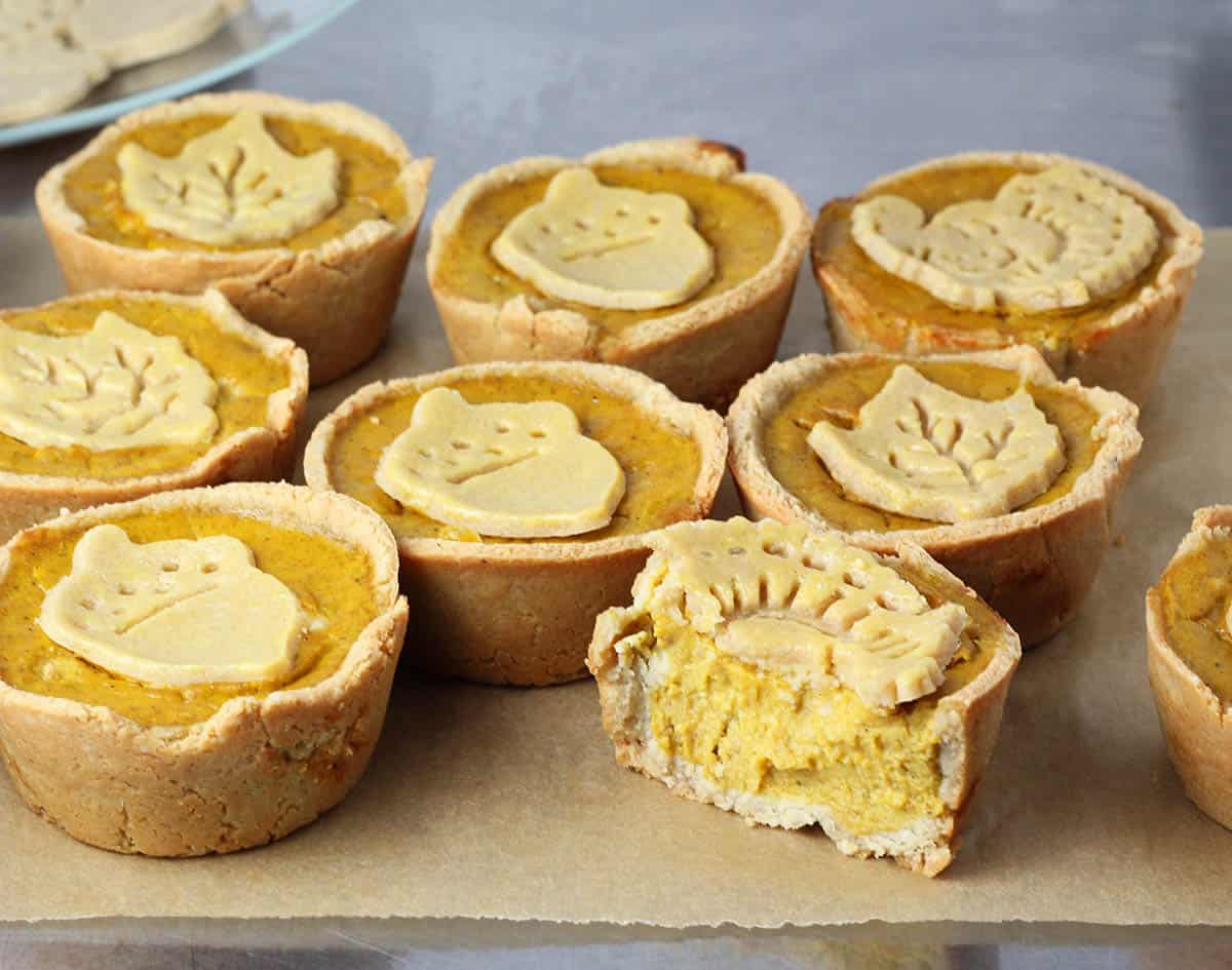 seven full and one half eaten mini pumpkin pies with fall shaped pie crust cookies on them on a sheet of unbleached parchment paper