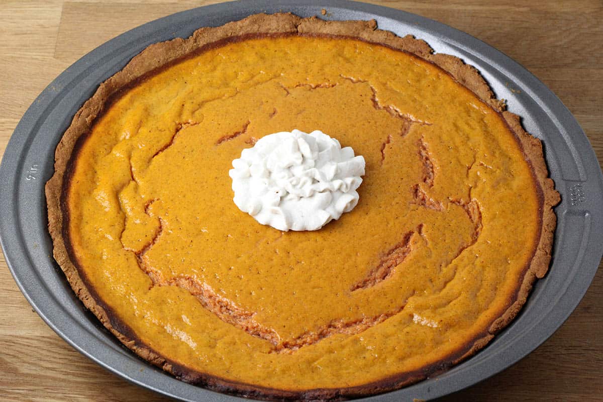 a full sweet potato pie with a swirl of cashew whipped cream in a metal pie pan on a wooden surface