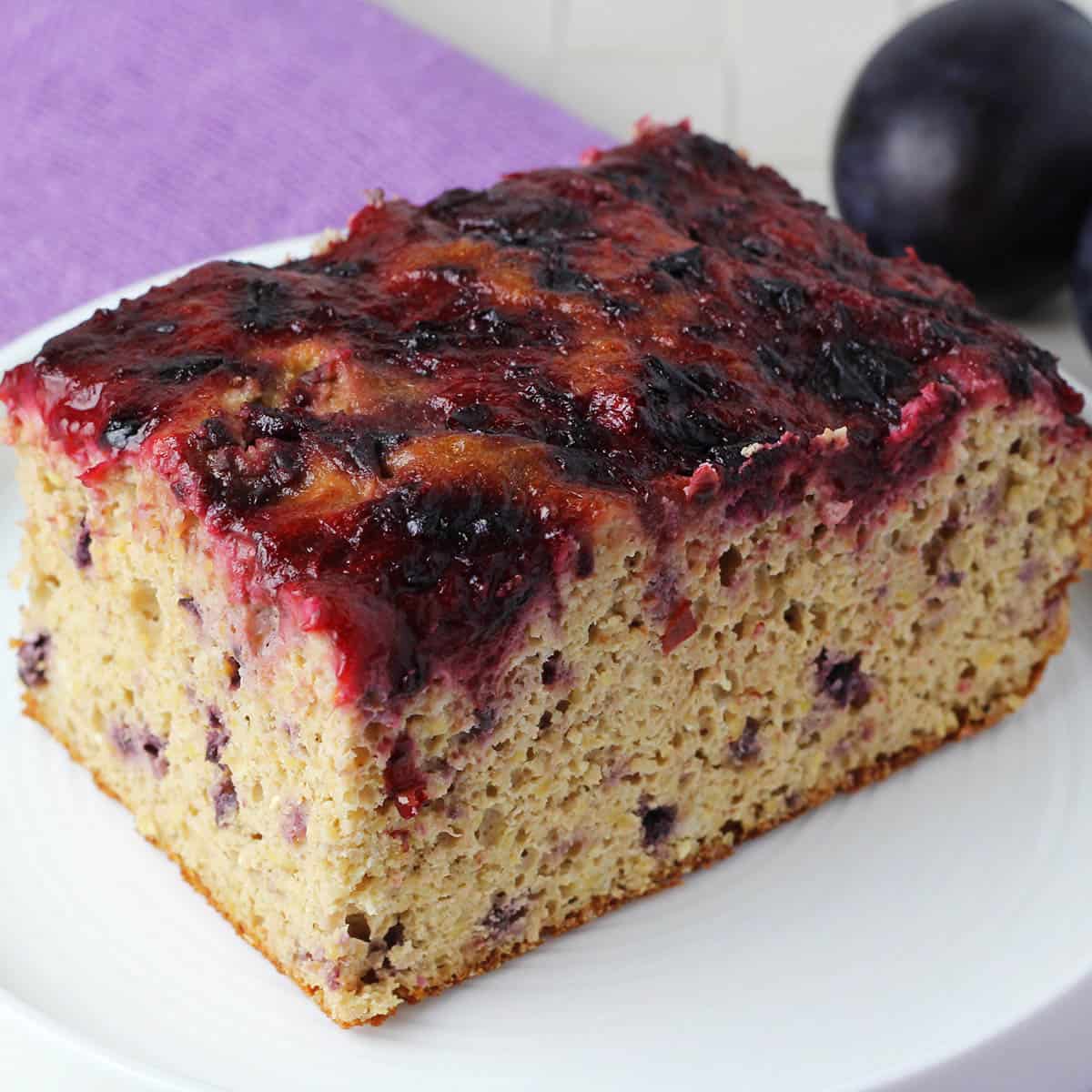 a rectangular piece of corn cake with plum sauce on top and a plum in the background