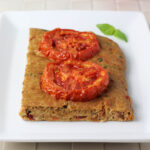 one piece of tomato basil focaccia with two slices of roasted tomato on top on a white plate
