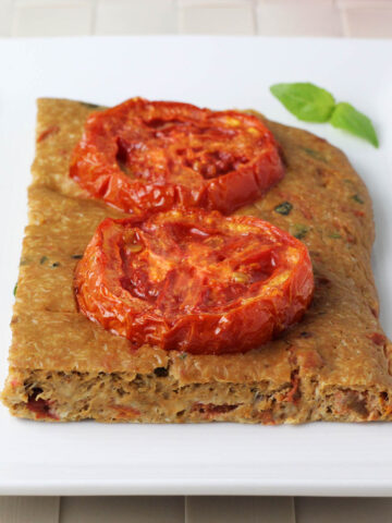 one piece of tomato basil focaccia with two slices of roasted tomato on top on a white plate