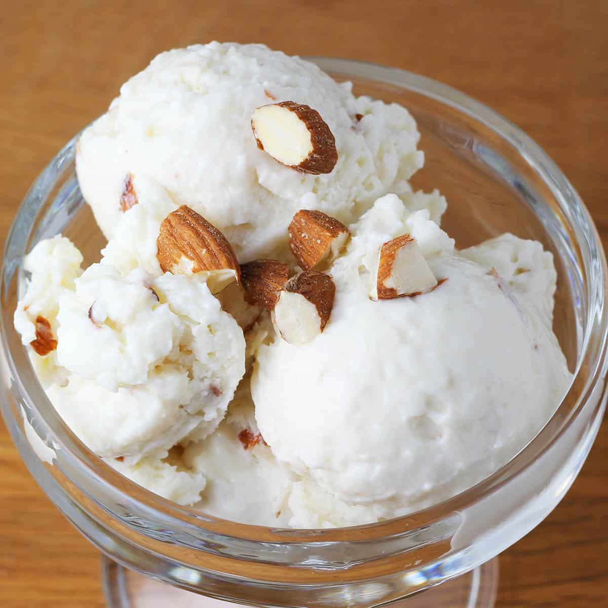 small glass dessert dish with vanilla protein ice cream and chopped almonds on a wood table