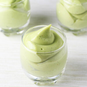 three servings of vanilla avocado mousse in shot glasses on a beige background