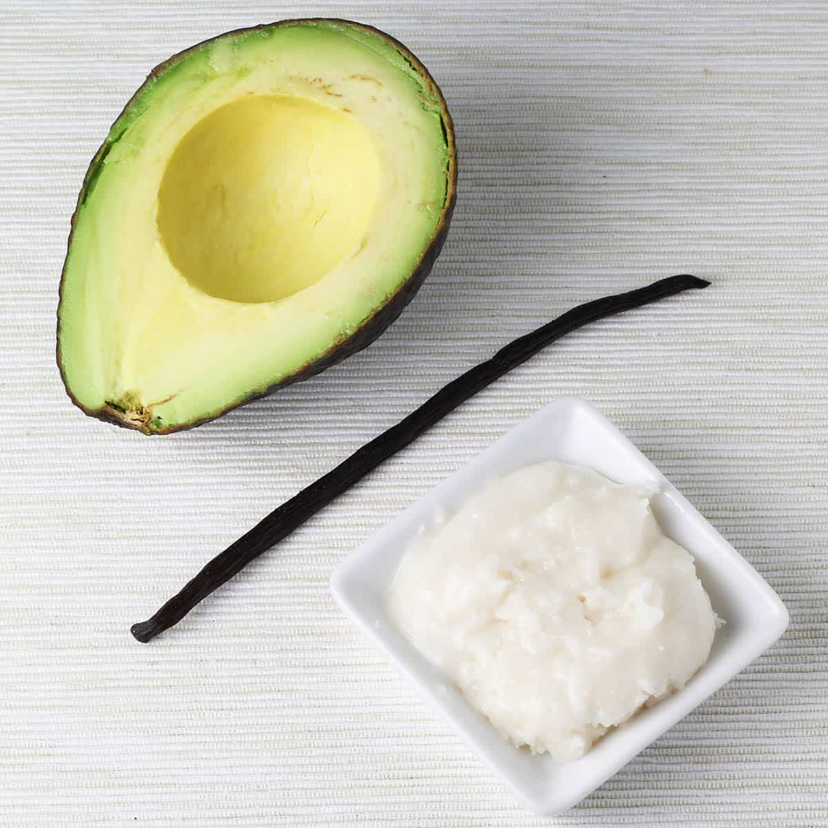 half avocado next to a vanilla bean and a small dish of coconut butter