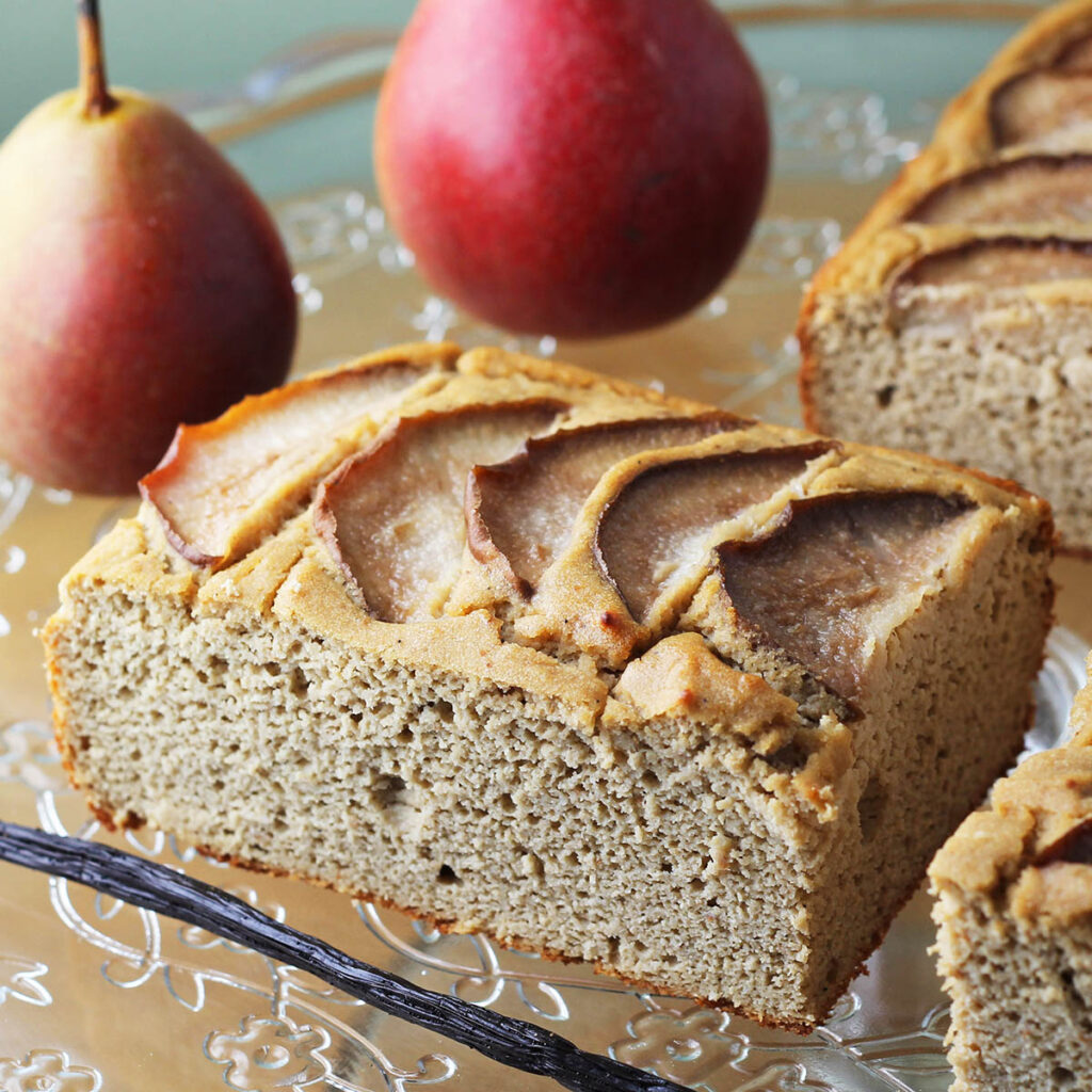 rectangular pice of vanilla pear protein cake with a vanilla bean in front an two pears in the background