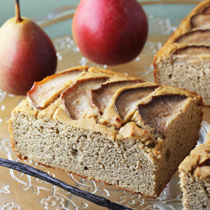 rectangular pice of vanilla pear protein cake with a vanilla bean in front an two pears in the background.