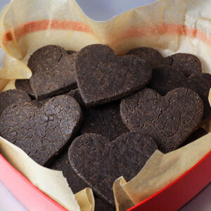 a heart shaped box lined with unbleached parchment paper and full of heart shaped chocolate vegan protein cookies