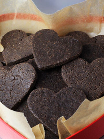 a heart shaped box lined with unbleached parchment paper and full of heart shaped chocolate vegan protein cookies