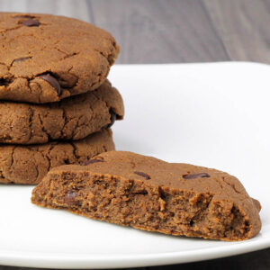 three full and one half chocolate pumpkin vegan cookies with chocolate chips on a white plate on a grey wood surface