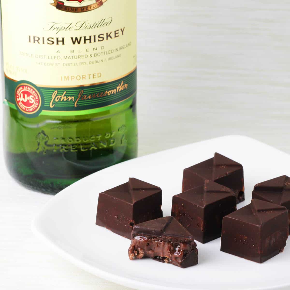 a white plate with several whisky filled chocolates in front of a bottle of Jameson Irish whisky on a light background