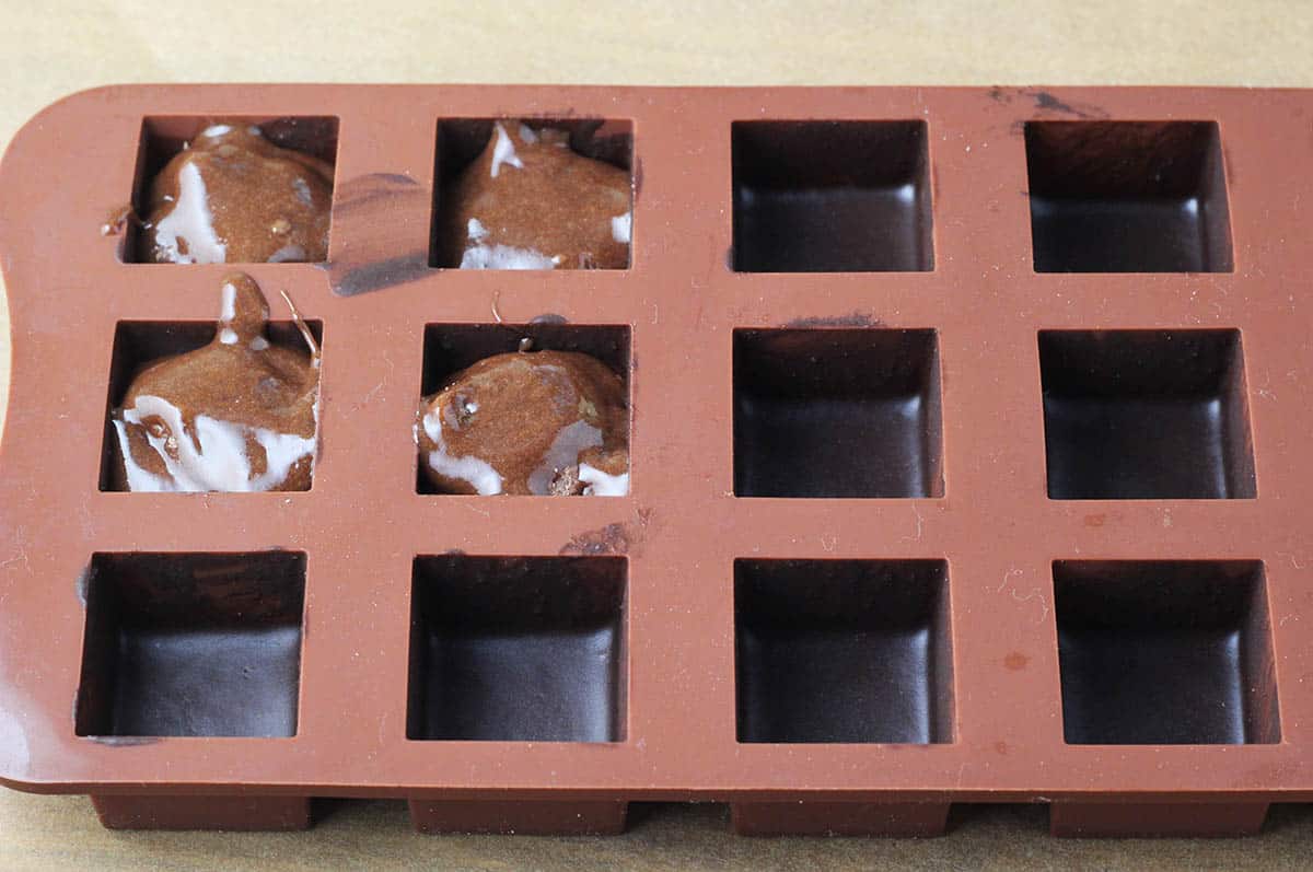 a brown silicone chocolate mold with cubic cavities that are lined with dark chocolate and some have a whisky filling also