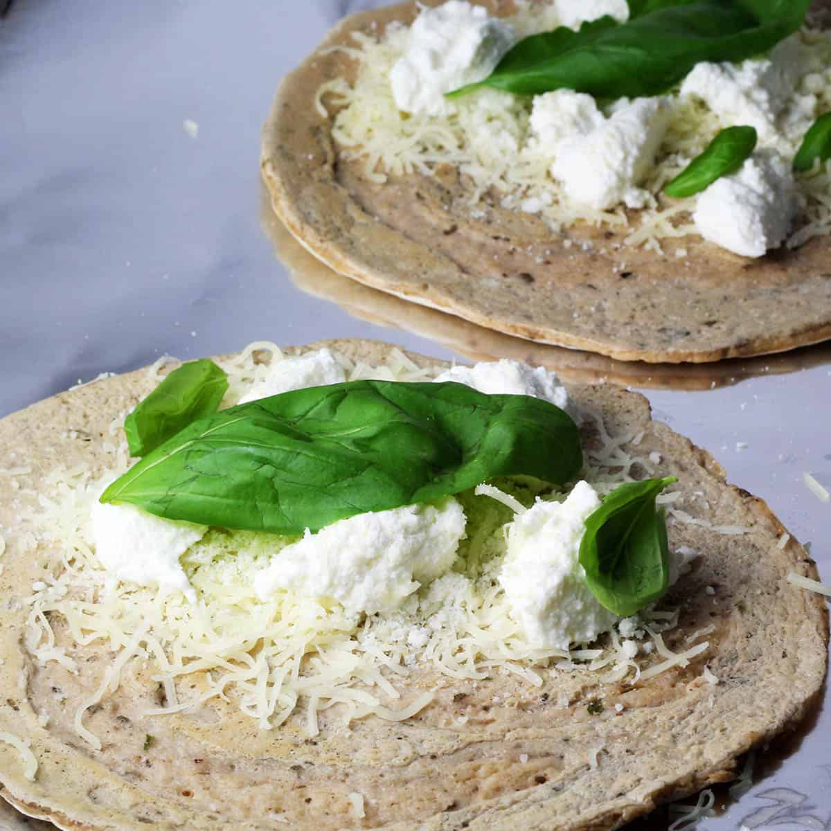 white protein pizza wraps before they are wrapped, with ricotta, mozzarella, and basil leaves