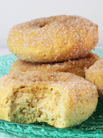 three full and one bitten vanilla cake donut covered in cinnamon erythritol on a bright green glass plate