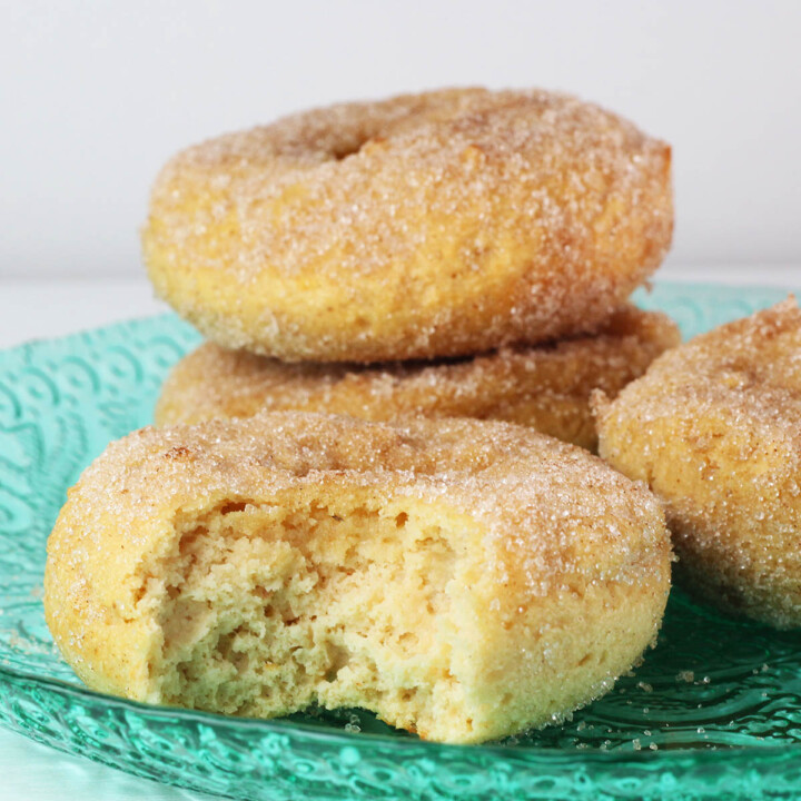 three full and one bitten vanilla cake donut covered in cinnamon erythritol on a bright green glass plate