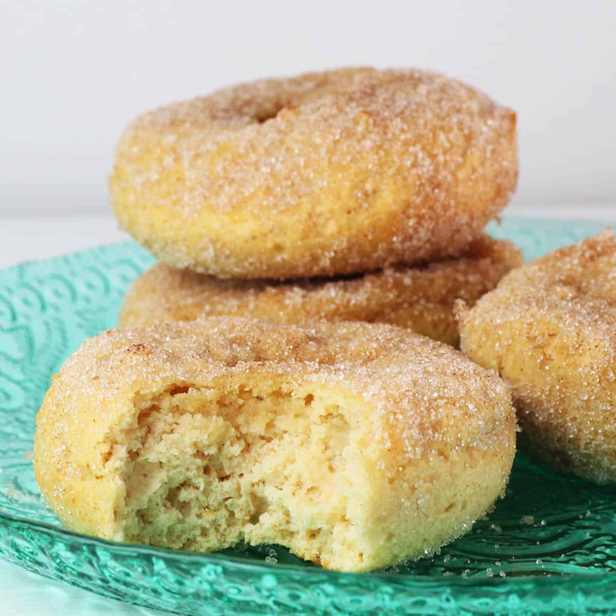 three full and one bitten vanilla cake donut covered in cinnamon erythritol on a bright green glass plate