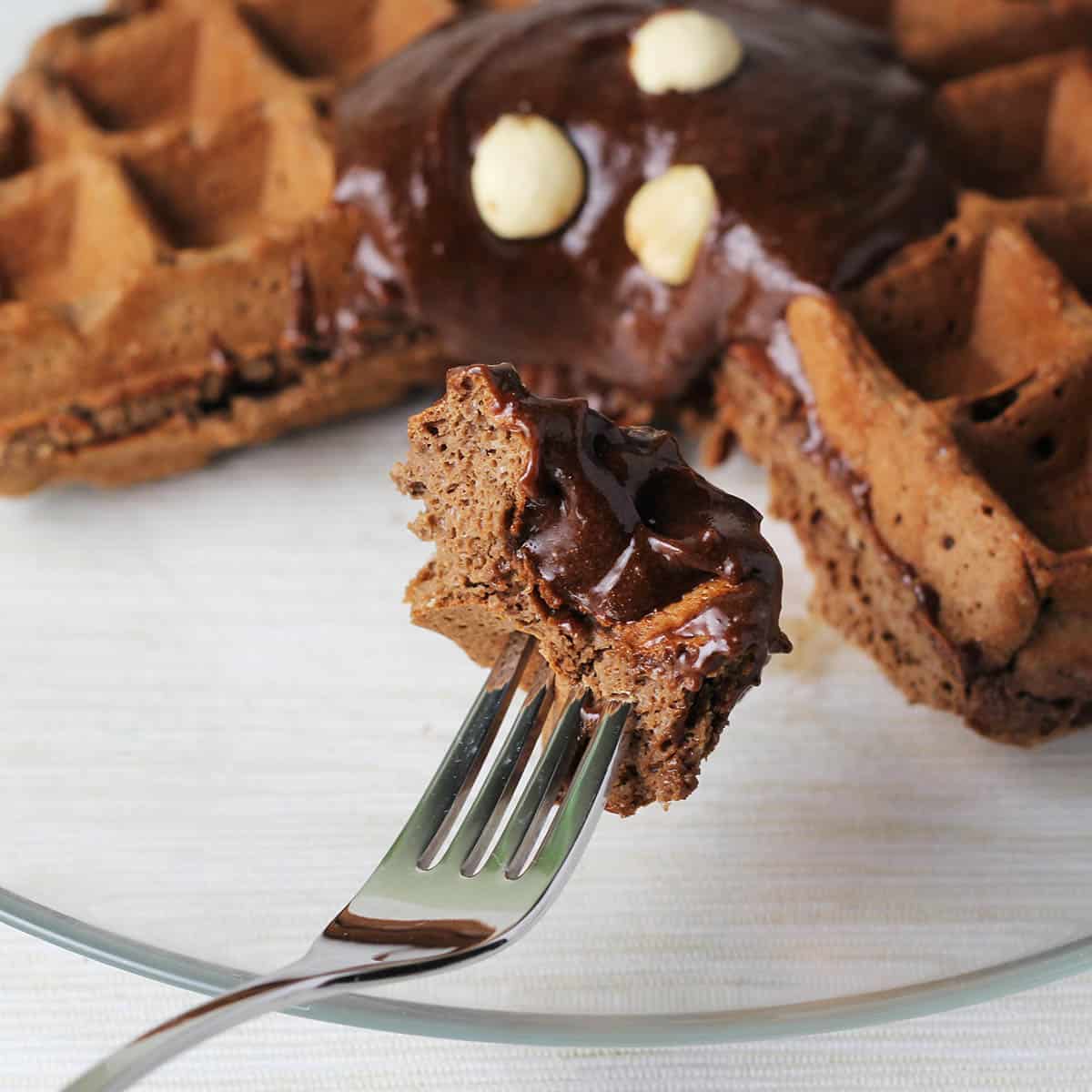 small piece of chocolate protein waffle on a fork in front of the rest of the large waffle
