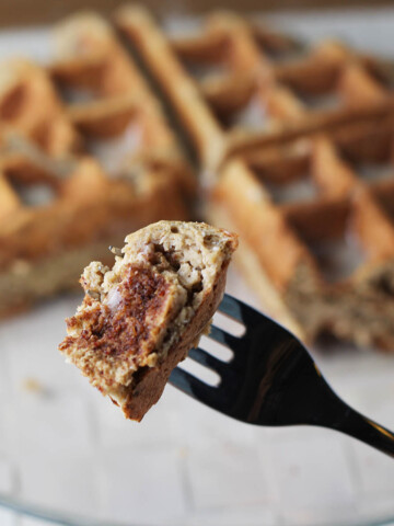bite of cinnamon protein waffle on a fork with the rest of the large waffle in the background