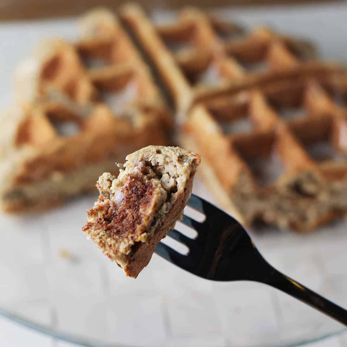 bite of cinnamon protein waffle on a fork with the rest of the large waffle in the background
