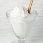 glass ice cream dish with coconut frozen yogurt and a wooden dessert spoon with a light background