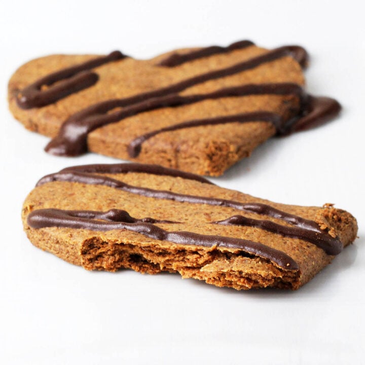 one full and one half heart shaped almond cookie with chocolate drizzle on a white background