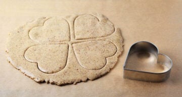 almond cookie dough with four heart shaped cookies cut into it, next to a heart shaped cookie cutter