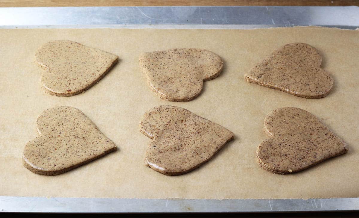 six unbaked heart shaped almond cookies on a parchment lined baking sheet