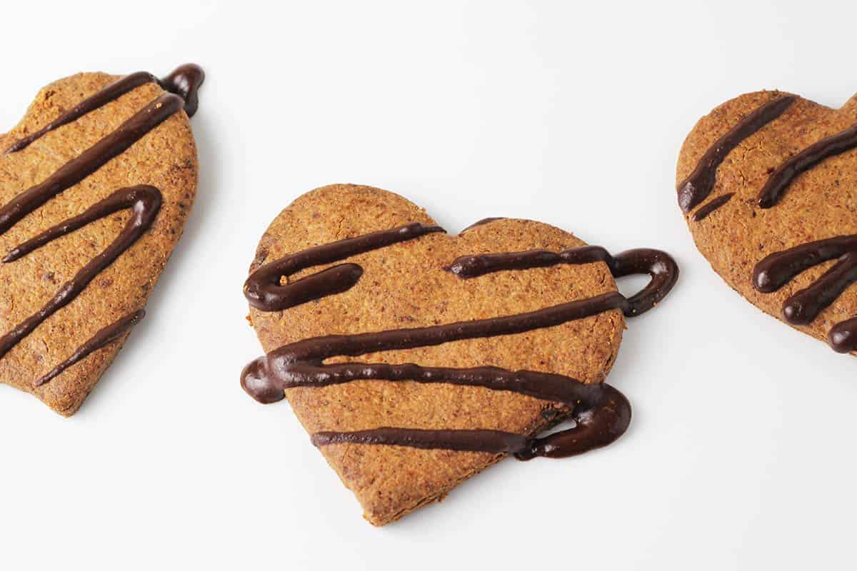 three heart shaped almond cookies with chocolate drizzle on a white plate