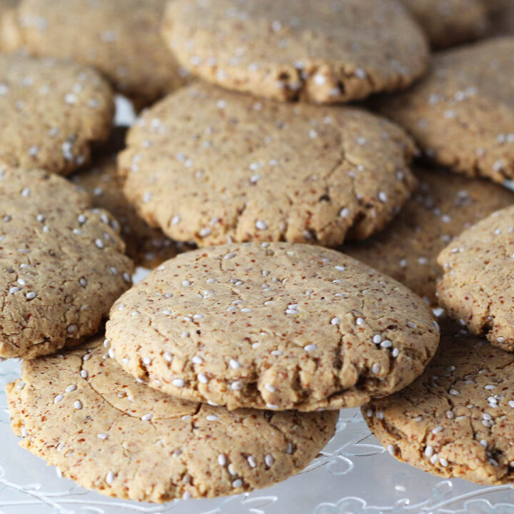 collection of round almond cookies with white chia seeds on a flower etched dessert plate