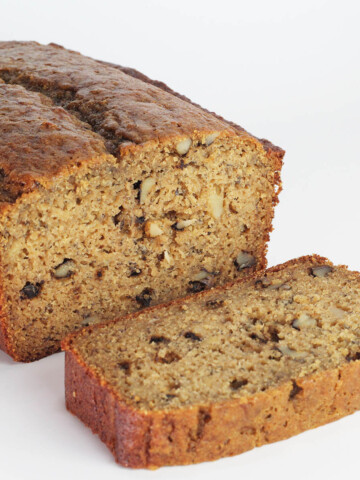loaf of banana nut bread with one slice down in front on a white backdrop