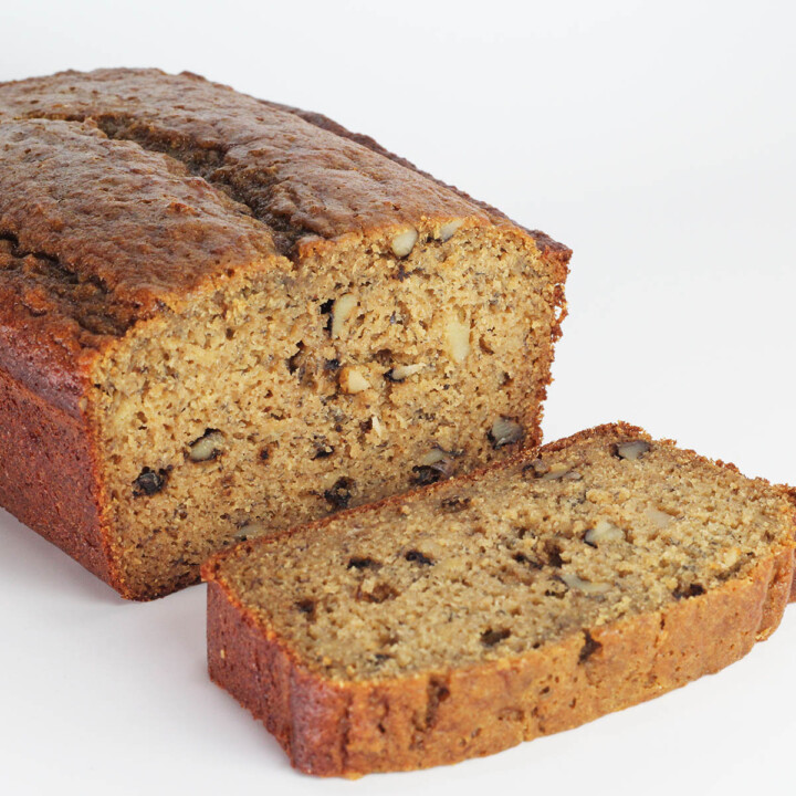 loaf of banana nut bread with one slice down in front on a white backdrop