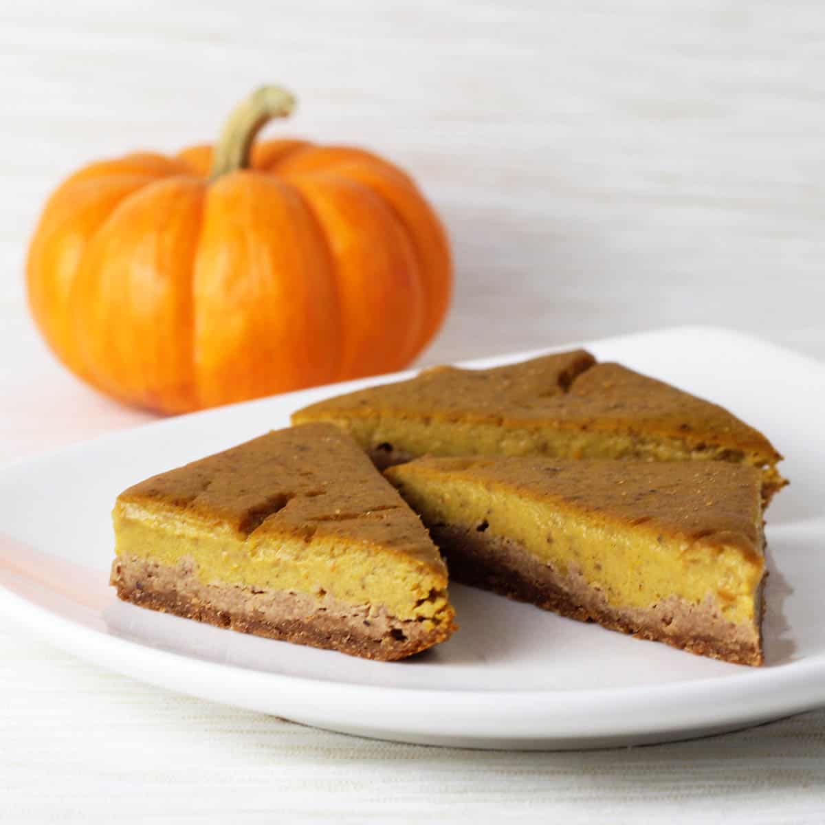 three triangular cut pumpkin pie bars on a white plate with an orange mini pumpkin behind it