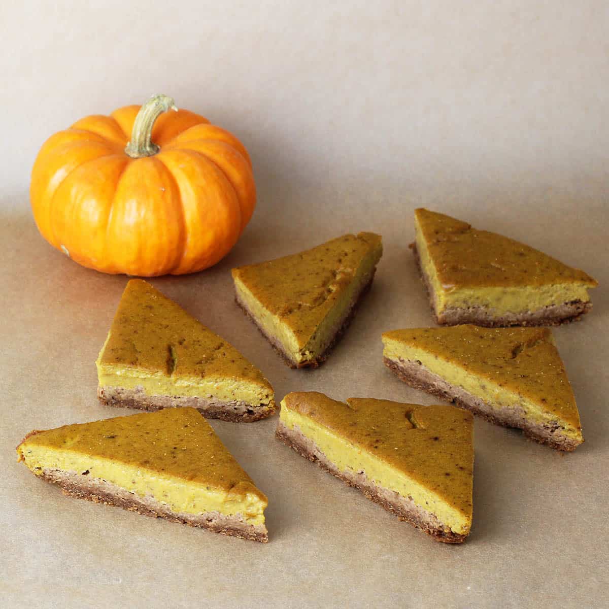 six triangular cut pumpkin pie bars and an orange mini pumpkin on an unbleached piece of parchment paper