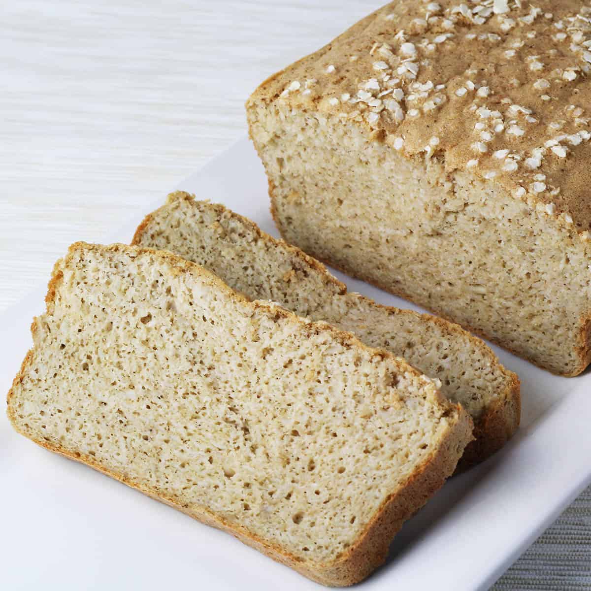 angled view of a loaf of maple quinoa protein bread with two slices down in front, all on a white plate on a light background