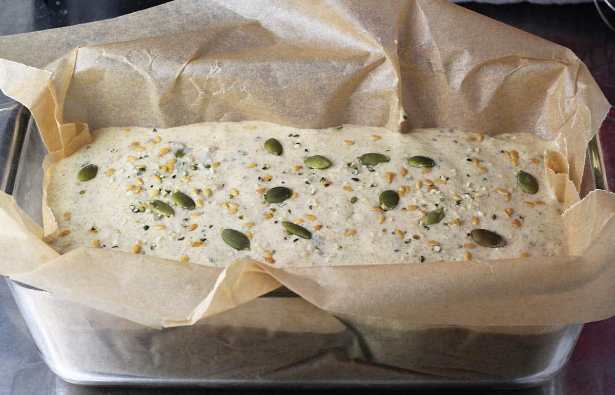 unbaked loaf of seeded bread in a parchment-lined glass loaf pan