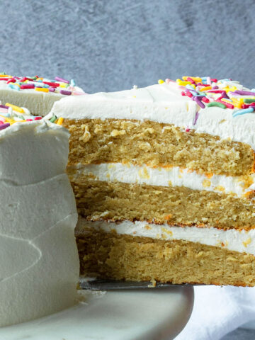 slice of frosted 3 layer cake being pulled out with a cake server, with a grey background