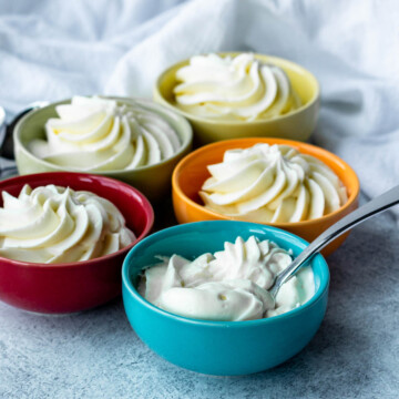 5 small dishes of various colors each with a serving of keto cheesecake mousse, and the one in the front has a spoon in it