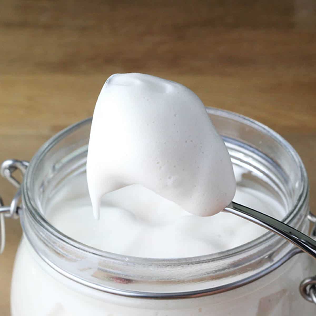 a spoonful of protein marshmallow fluff being pulled up from the jar on a wood table