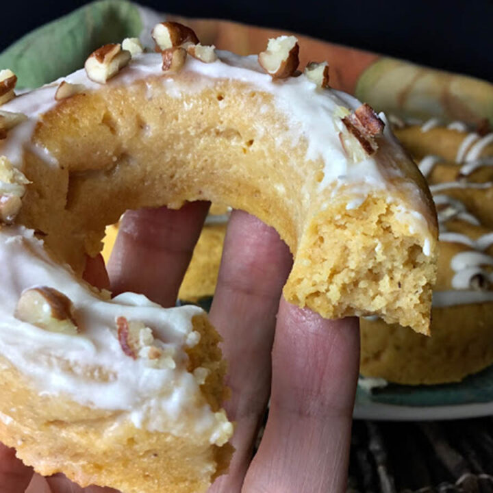 donut in hand, bitten and topped with icing and pecans