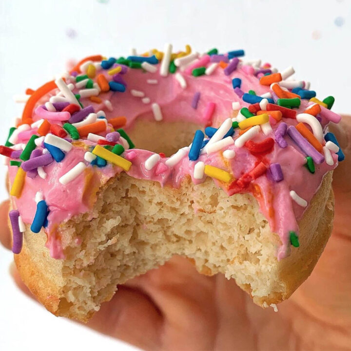 bitten donut in hand, with pink frosting and colored sprinkles