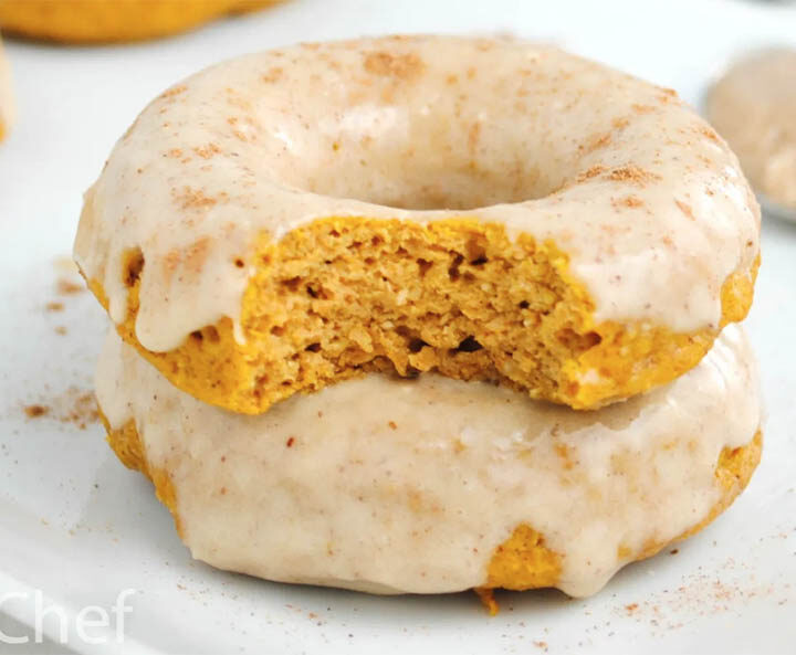 two iced gingerbread donuts stacked, with the top one missing a bite